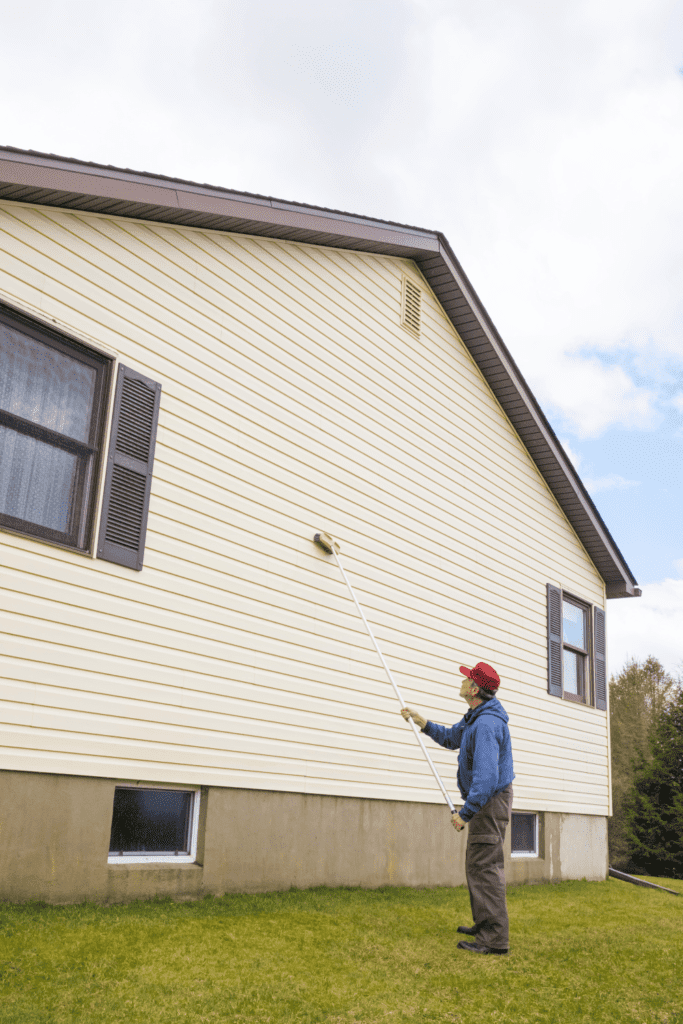 A man in blue jacket painting the side of house.