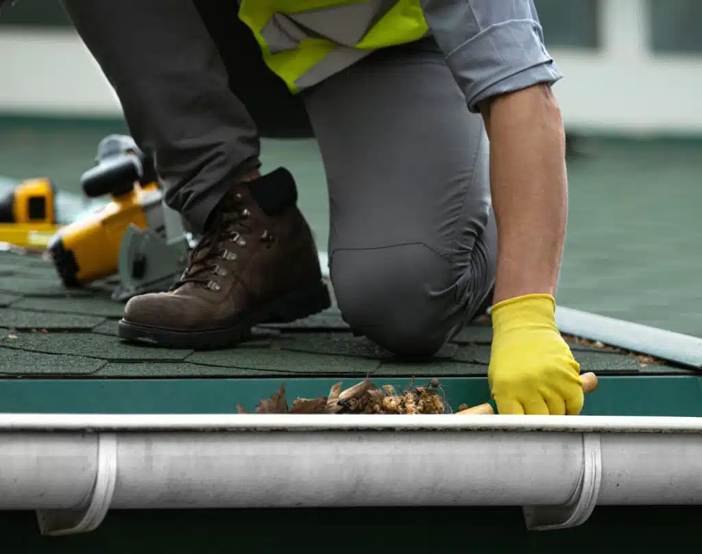 A person in yellow gloves is working on the gutter.